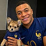 Belle participe au concours pour gagner de l'argent avec cette photo : man, dog, puppy, smiling, portrait, indoor, blue_jersey, french_team, sportswear, holding, cute, pet, face, watch, short_hair, happy, animal, friendship, casual, background