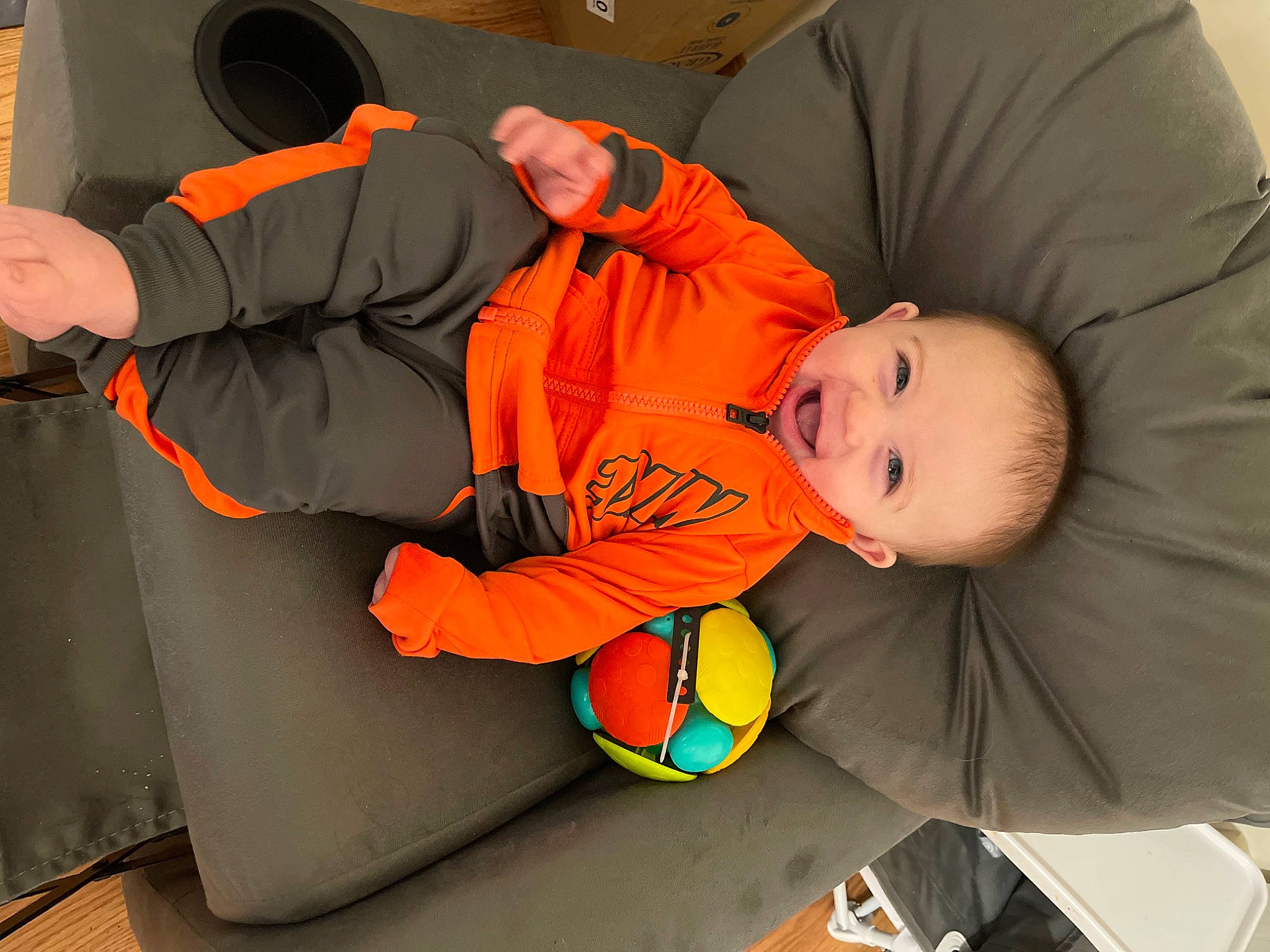 Wilder is registered to the contest to win money with this photo: baby, baby_toddler_clothing, child, comfort, flooring, fun, gesture, orange, person, personal_protective_equipment, room, sitting, sleeve, smile, thumb, toddler