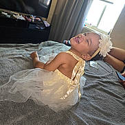 Adhara is registered to the contest to win money with this photo: adult, baby, bed, bedroom, blanket, celebration, child, curtains, dress, flower_headband, hand, happy, headband, indoor, infant, laughing, portrait, smiling, television, window