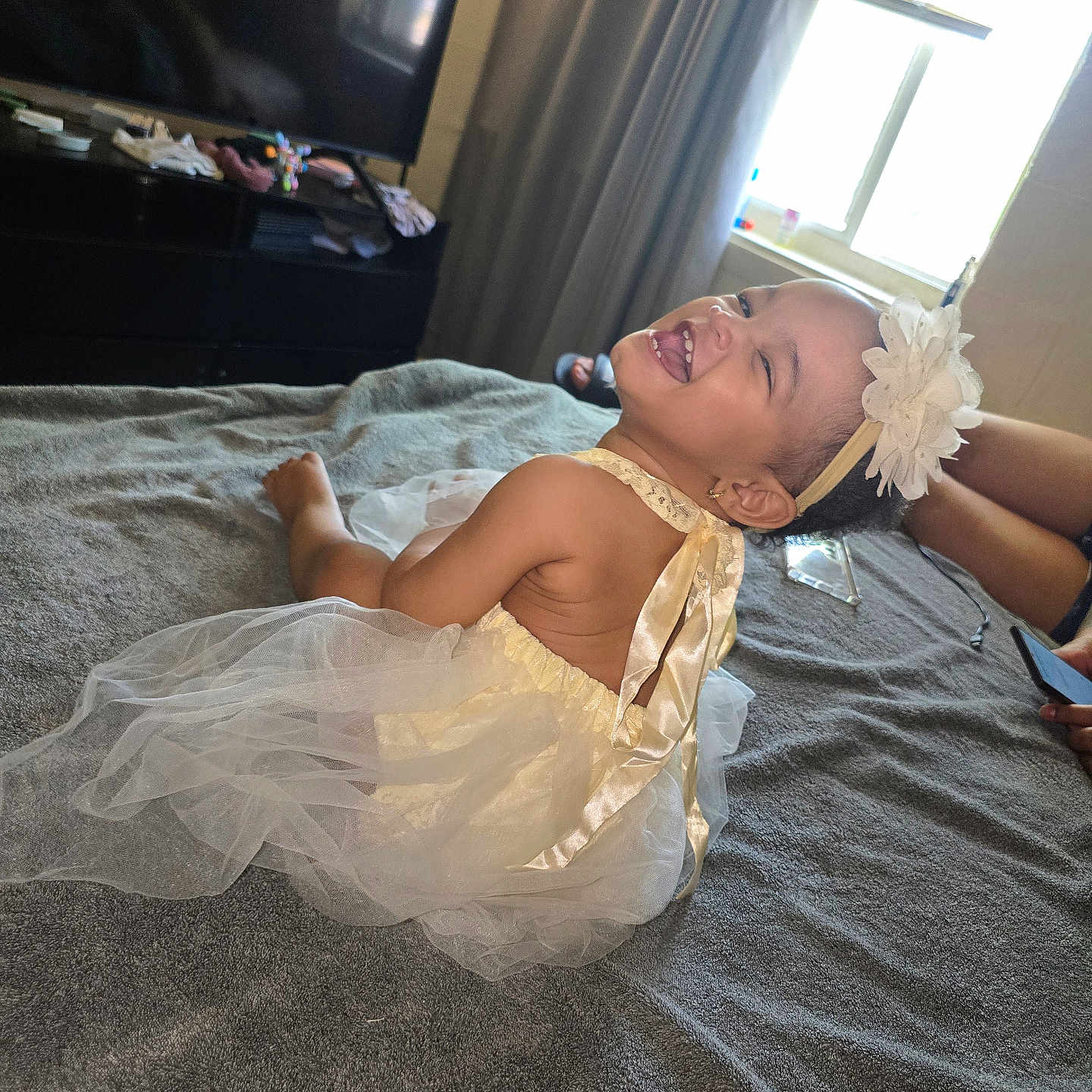 Adhara is registered to the contest to win money with this photo: adult, baby, bed, bedroom, blanket, celebration, child, curtains, dress, flower_headband, hand, happy, headband, indoor, infant, laughing, portrait, smiling, television, window