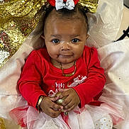 Kalyiah joined the competition — help win amazing prizes! baby, infant, child, gold_bow, red_shirt, tutu, gold_glitter, necklace, bracelet, ornament, smile, big_eyes, portrait, sitting, fabric, festive, holiday, cute, hands, soft_background