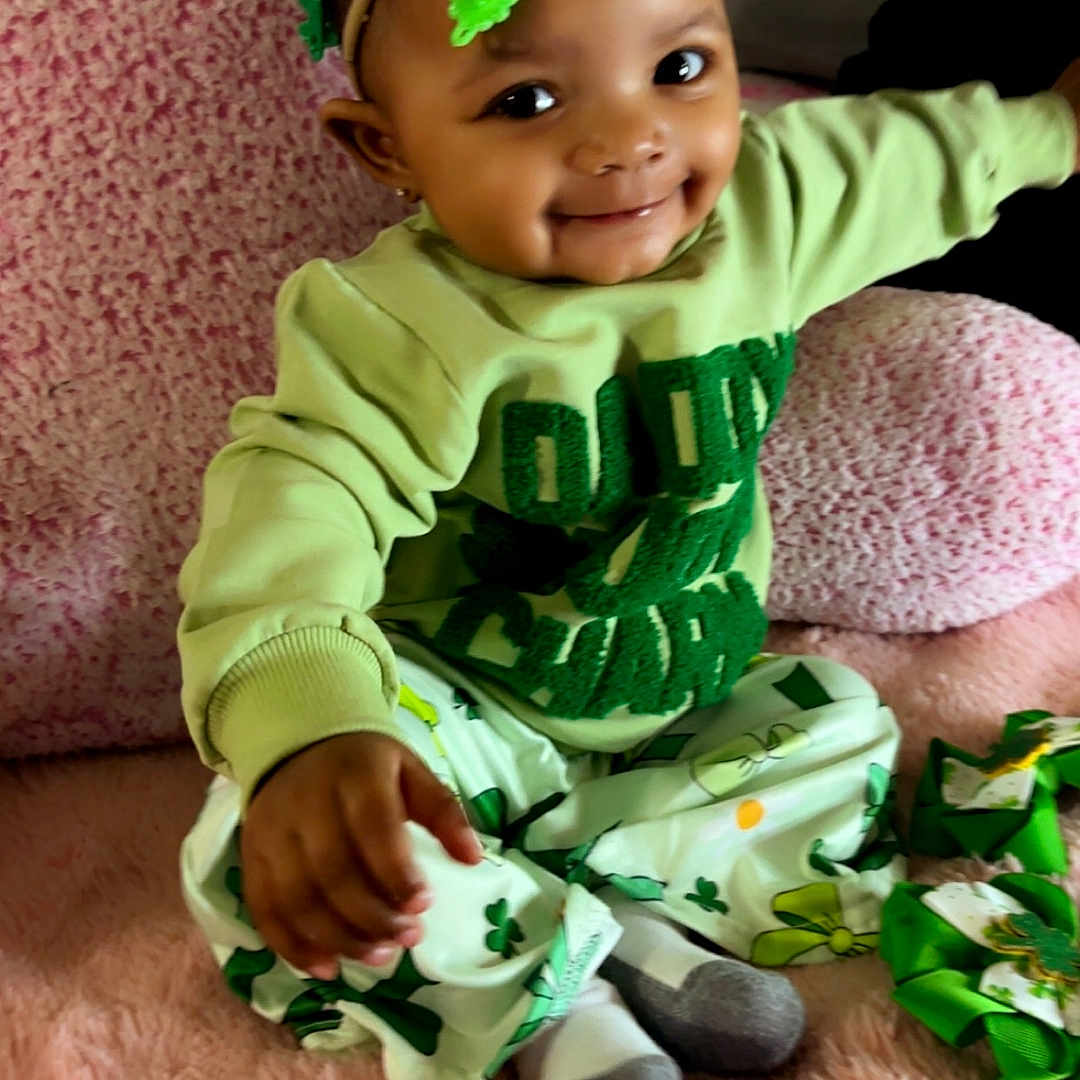 Kalyiah is registered to the contest to win money with this photo: baby, infant, toddler, smiling, dimples, headband, bow, clover, shamrock_pattern, green_outfit, green_clothing, pink_blanket, plush_blanket, sitting, socks, hand_reaching, portrait, cute, bedroom, adorable