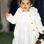 toddler, child, white_dress, quilted_jacket, outdoor, grass, dog, pet, curly_hair, portrait, person, cute, young_child, winter_clothing, standing, animal, background_people, fashion, happy, innocent