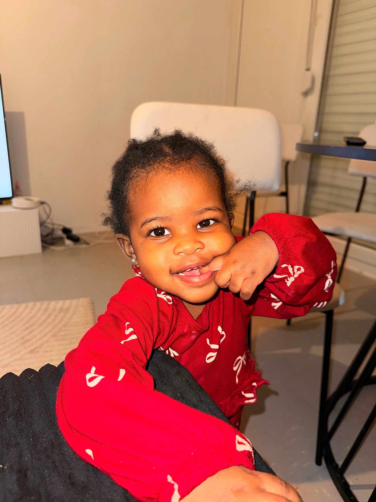 Fatoumata-Zahra a rejoint le concours — aidez-le/la à gagner de superbes lots ! child, toddler, smile, red_clothing, long_sleeve, finger_in_mouth, hand, eyes, earrings, hair, indoor, chair, table, rug, floor, portrait, happy, flash_lighting, home_interior, person