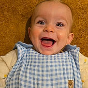 Loé a rejoint le concours — aidez-le/la à gagner de superbes lots ! baby, infant, smiling, laughing, happy, face, eyes, mouth, tongue, teeth, bib, blue_gingham, checkered_pattern, brown_towel, background, onesie, clothing, closeup, indoor, cheerful