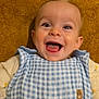 baby, infant, smiling, laughing, happy, face, eyes, mouth, tongue, teeth, bib, blue_gingham, checkered_pattern, brown_towel, background, onesie, clothing, closeup, indoor, cheerful