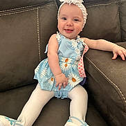 Kourtney is registered to the contest to win money with this photo: baby, bonnet, cap, clothing, couch, cushion, dress, face, footwear, furniture, happy, hat, head, pants, person, photography, portrait, shoe, sitting, sneaker