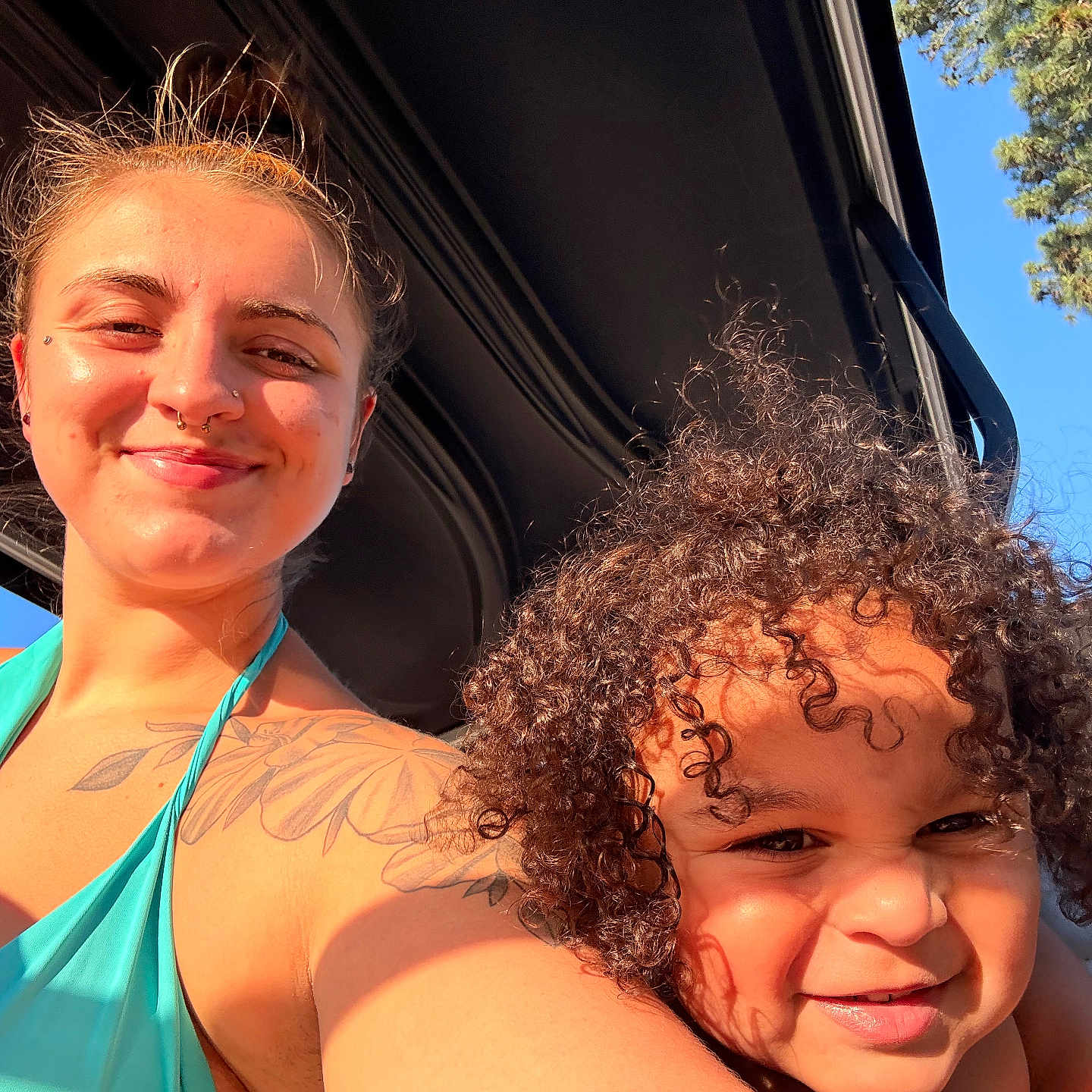 Kashton Purcell is registered to the contest to win money with this photo: woman, child, smile, tattoo, curly_hair, sunlight, outdoor, blue_sky, tree, vehicle, portrait, happy, skin, face, shoulder, daylight, casual, people, nature, summer