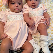 De'Naja De'nae Hines joined the competition — help win amazing prizes! baby, infant, twins, matching_outfits, pink_dress, headbands, bows, white_shoes, ruffled_socks, blanket, pillow, paisley_pattern, closeup, portrait, holding_hands, serious_expression, chubby_cheeks, indoor, sitting, cute