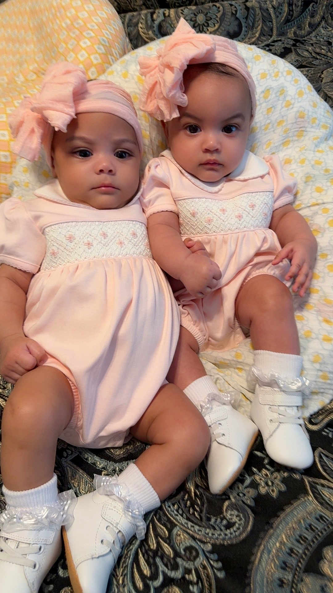 De'Naja De'nae Hines joined the competition — help win amazing prizes! baby, infant, twins, matching_outfits, pink_dress, headbands, bows, white_shoes, ruffled_socks, blanket, pillow, paisley_pattern, closeup, portrait, holding_hands, serious_expression, chubby_cheeks, indoor, sitting, cute
