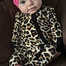 Riley Faye is registered to the contest to win money with this photo: baby, infant, headband, pink_bow, leopard_print, onesie, couch, brown_furniture, barefoot, foot, face, blue_eyes, curious_expression, seated, indoors, child, cute, portrait, young_child, comfortable