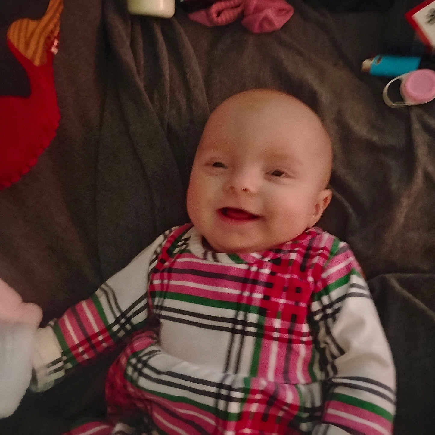 Shaina joined the competition — help win amazing prizes! baby, smile, infant, striped_clothing, blanket, indoor, child, happy, person, face, cute, lying_down, plaid_pattern, soft_toys, bottle, pink, red, green, white, cozy