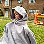 toddler, child, hoodie, gray_hoodie, grass, outdoor, brick_house, side_view, pensive, oversized_clothing, casual, young_child, greenery, suburban, caution_barrier, curtains, windows, face, portrait, daylight