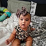 Janae is registered to the contest to win money with this photo: baby, child, infant, bow, leopard_print, clothing, bed, pillow, blanket, pattern, indoor, cute, sitting, person, headband, footwear, expression, skin, young, portrait