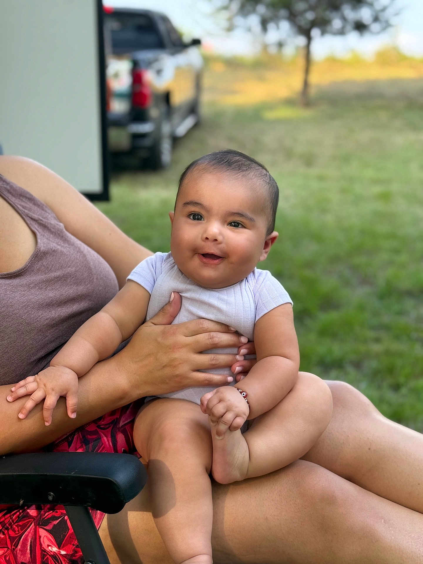 Janae joined the competition — help win amazing prizes! baby, child, smile, happy, arm, hand, outdoor, grass, tree, person, skin, sitting, clothing, bracelet, leg, foot, holding, chair, adult, daylight
