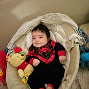 Nathanael is registered to the contest to win money with this photo: baby, infant, baby_seat, plush_toy, winnie_the_pooh, black_clothing, red_clothing, smiling, indoors, cute, child, soft_toys, cozy, happy, feet, face, person, comfort, resting, casual