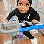 child, toddler, shopping_cart, black_beanie, black_sweater, white_shoes, store_aisle, curious, wide_eyes, holding, clothing, floor, shopping, person, indoor, retail, casual, cute, portrait, young