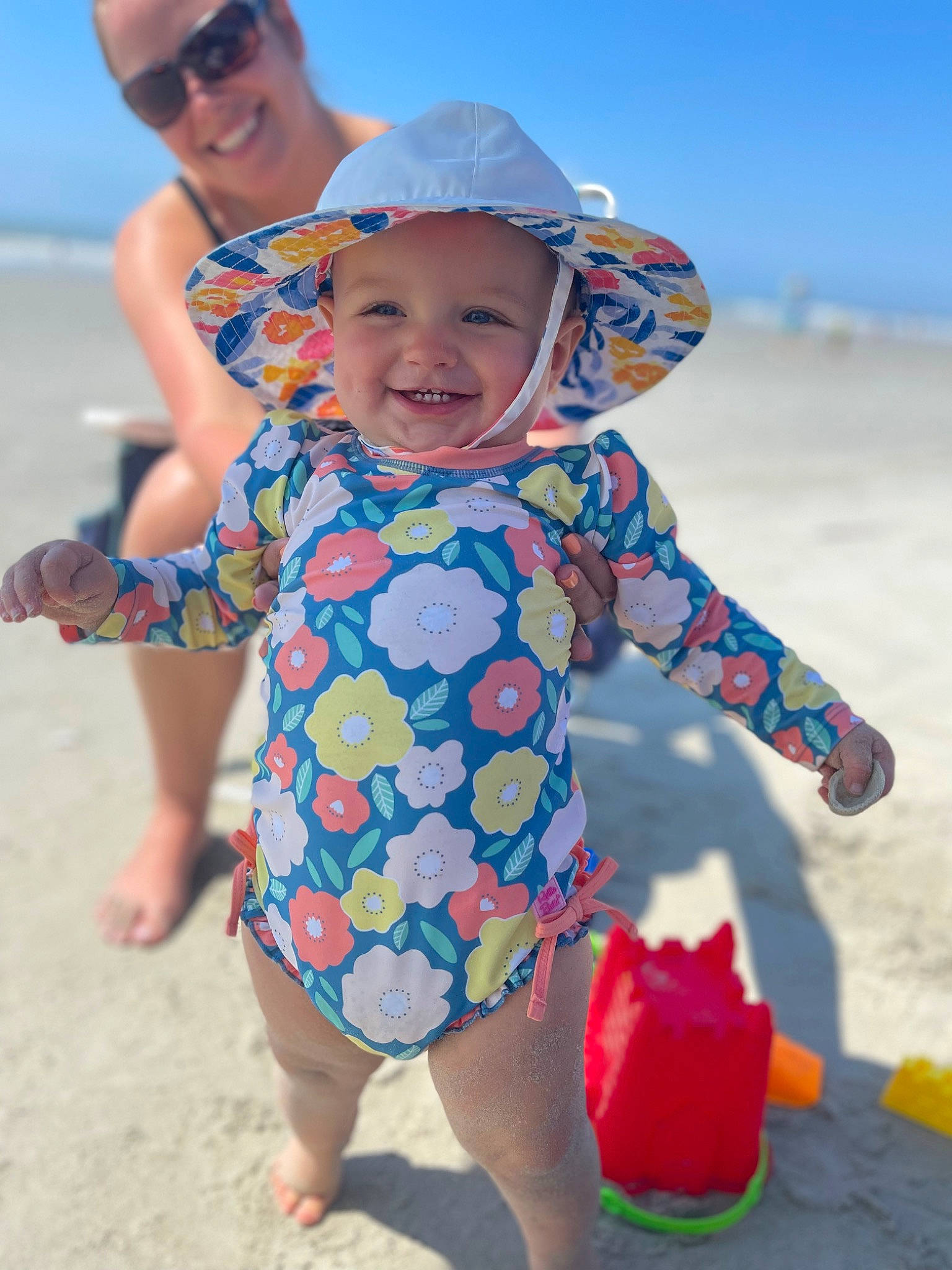 Olive is registered to the contest to win money with this photo: azure, baby_toddler_clothing, beach, blue, body_of_water, fun, goggles, happy, hat, headgear, headwear, joy, people_in_nature, people_on_beach, person, photograph, sky, sleeve, smile, sun_hat