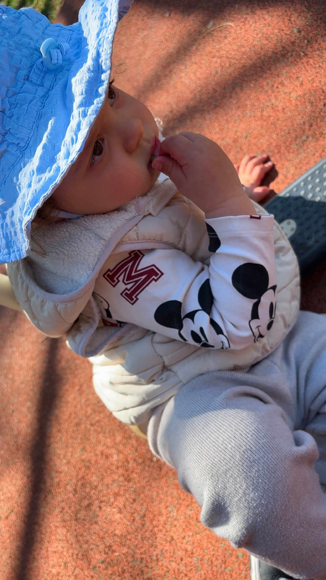 Lorenzo participe au concours pour gagner de l'argent avec cette photo : child, toddler, baby, sun_hat, blue_hat, vest, mickey_mouse, sleeve, hand, fingers, face, eyes, outdoor, playground, rubber_surface, shadow, clothing, pants, sitting, cute