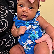 Zaylee joined the competition — help win amazing prizes! baby, infant, child, headband, bow, blue_clothing, floral_pattern, hand, skin, smiling_face, black_shirt, smiley_face, person, cute, portrait, indoors, holding, closeup, expression, human