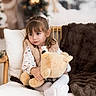 Kiara participe au concours pour gagner de l'argent avec cette photo : blanket, bokeh, brown_hair, chair, child, christmas_tree, cozy, dress, fringe_bangs, fur_throw, girl, holiday, indoor, pillow, plush_toy, portrait, soft_lighting, teddy_bear, vest, white_tights