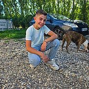 Edzio a rejoint le concours — aidez-le/la à gagner de superbes lots ! boy, brindle_dog, car, child, crouching, dog, gravel, greenery, happy, jeans, outdoors, parked_car, pet, portrait, smile, sneakers, sunlight, trees, tshirt, wristwatch