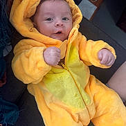 Beau joined the competition — help win amazing prizes! baby, child, costume, duck_costume, yellow, plush, hood, couch, furniture, indoor, person, infant, cute, smile, raised_fist, soft_texture, warm_clothing, portrait, cozy, funny