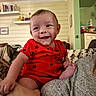Beau is registered to the contest to win money with this photo: baby, smile, red_clothing, indoor, person, face, hand, foot, dog, furniture, shelf, book, wall, home_interior, couch, happy, child, portrait, warm_lighting, casual