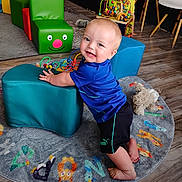 Riot joined the competition — help win amazing prizes! toddler, child, smiling, blue_shirt, black_shorts, colorful_rug, animal_rug, cushioned_block, toy, wooden_floor, indoor, playroom, bead_maze, white_chairs, happy, kneeling, person, furniture, floor, play