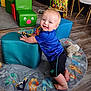toddler, child, smiling, blue_shirt, black_shorts, colorful_rug, animal_rug, cushioned_block, toy, wooden_floor, indoor, playroom, bead_maze, white_chairs, happy, kneeling, person, furniture, floor, play