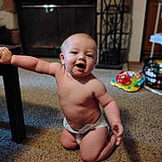 Riot is registered to the contest to win money with this photo: baby, child, diaper, indoor, carpet, table, furniture, toy, play, kneeling, smiling, happy, face, skin, room, home, person, infant, cute, young