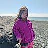 casual_clothing, child, colorful_leggings, daylight, girl, happy, leisure, nature, ocean, outdoor, pebbles, pink_jacket, portrait, rocky_beach, sky, smiling, standing, vacation, windy, young