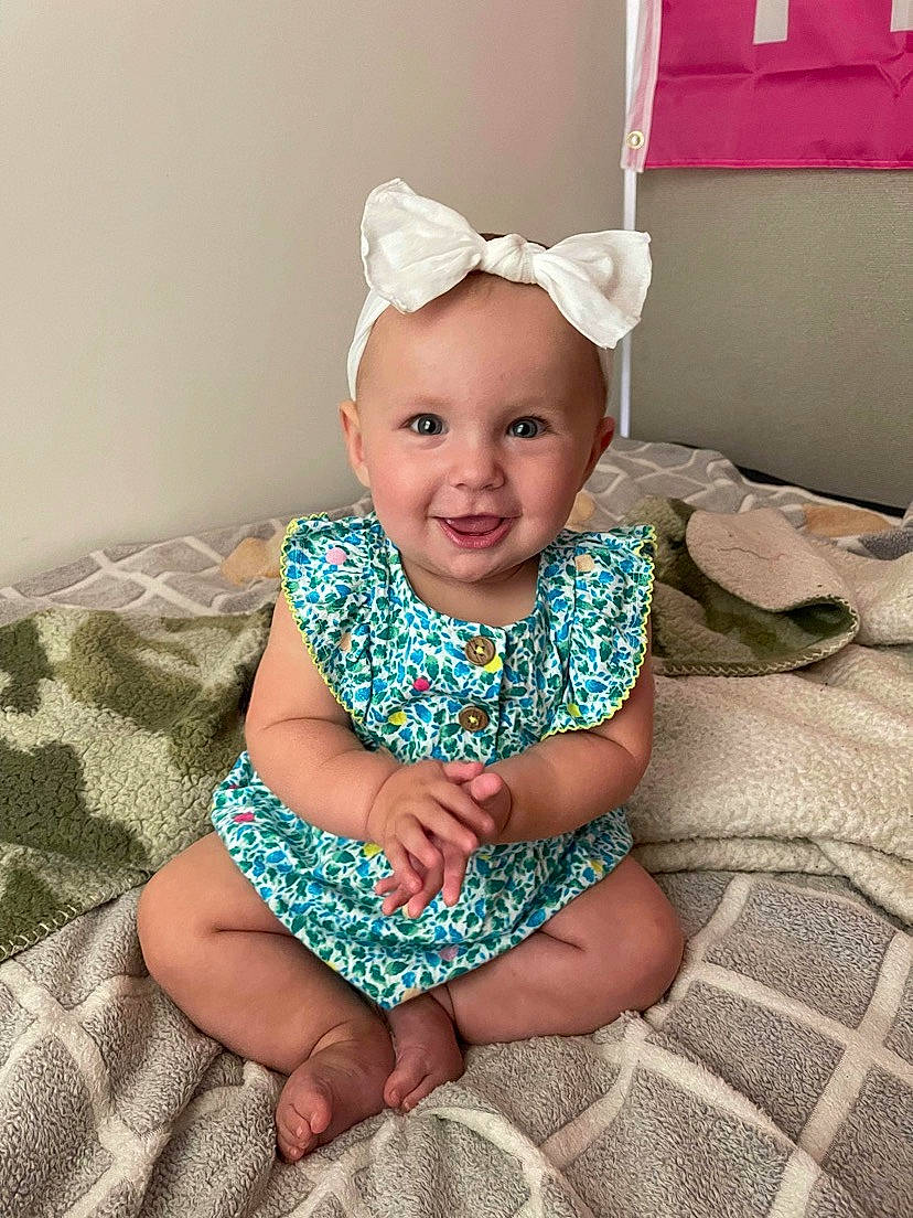 Averie is registered to the contest to win money with this photo: arm, baby_toddler_clothing, chin, dress, eye, face, facial_expression, flash_photography, happy, head, headgear, human_body, iris, joy, person, pink, purple, skin, sleeve, smile