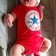 Vinnie is registered to the contest to win money with this photo: apparel, baby, child, closeup, converse, cushion, cute, footwear, hat, headwear, indoors, infant, lying_down, person, playful, red_clothing, skin, smiling, socks, tongue_out
