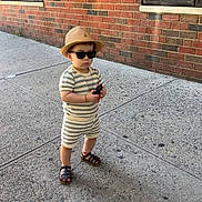 Noah joined the competition — help win amazing prizes! child, toddler, outdoor, sidewalk, brick_wall, building, sunglasses, sun_hat, striped_clothing, romper, sandals, toy, standing, portrait, urban, daylight, fashion, cute, person, street
