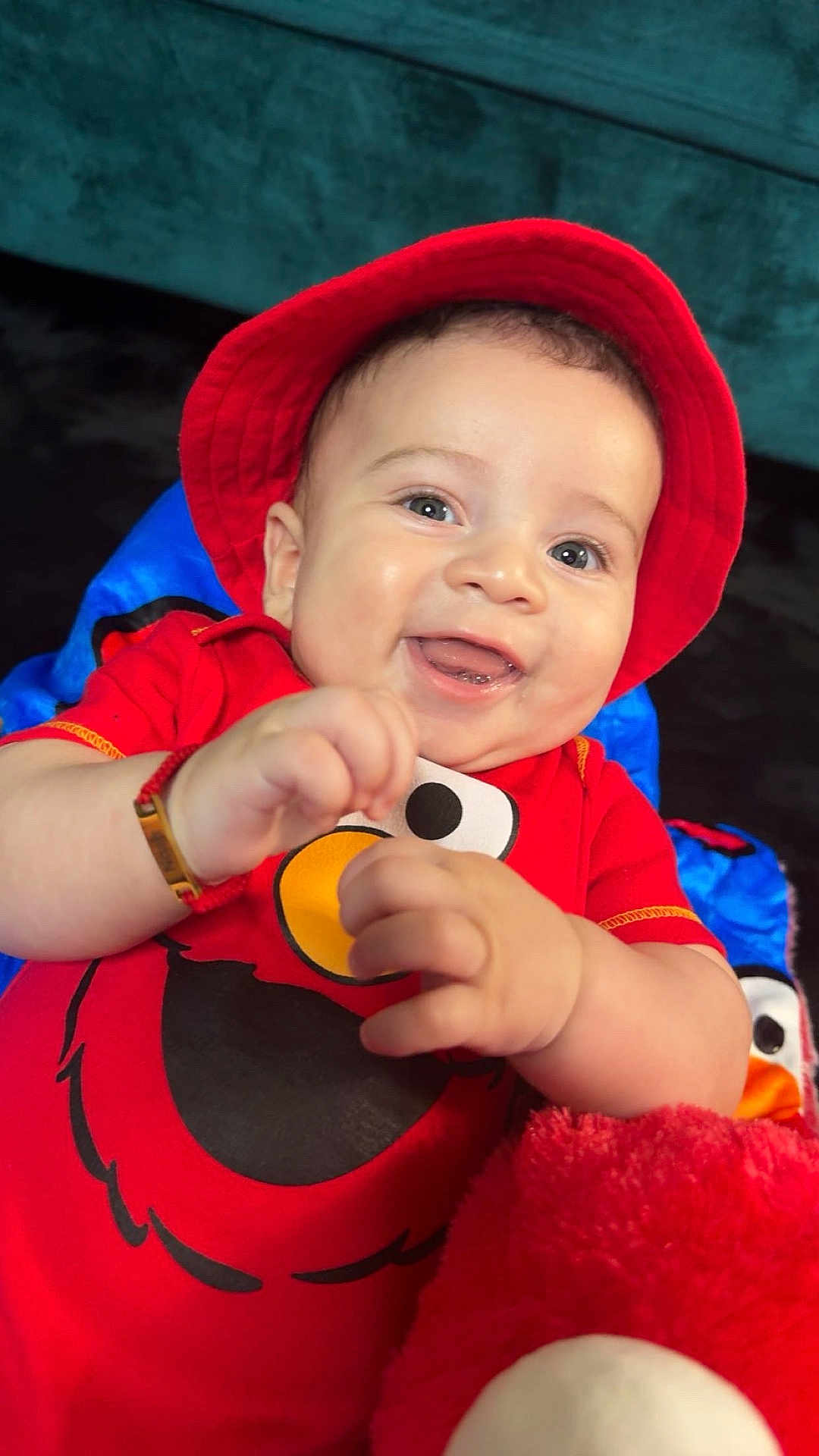 Noah is registered to the contest to win money with this photo: baby, child, smiling, red_hat, elmo_shirt, plush_toy, happy, cute, portrait, indoor, closeup, face, hands, infant, red_clothing, playing, fun, joy, bright_colors, soft_toy