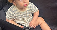 Noah is registered to the contest to win money with this photo: baby, child, toddler, stroller, hat, straw_hat, striped_shirt, sandals, necklace, sitting, face, portrait, outdoor, pavement, travel, vehicle, infant, fashion, looking_away, casual