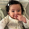 Angelina is registered to the contest to win money with this photo: baby, infant, child, portrait, smiling, happy, curly_hair, dark_hair, finger_in_mouth, hand, floral_clothing, onesie, white_clothing, sitting, indoor, patterned_background, baby_seat, close_up, face, cozy