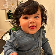 Angelina joined the competition — help win amazing prizes! baby, child, infant, portrait, smiling, happy, curly_hair, dark_hair, facial_expression, sitting, blue_outfit, ruffled_clothing, long_sleeves, fist, indoor, home, orchid, flowers, table, blanket