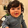baby, child, infant, portrait, smiling, happy, curly_hair, dark_hair, facial_expression, sitting, blue_outfit, ruffled_clothing, long_sleeves, fist, indoor, home, orchid, flowers, table, blanket