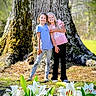 children, girls, smiling, tree_trunk, flowers, lilies, nature, outdoor, grass, plants, sunlight, friendship, casual_clothing, happy, portrait, spring, daylight, greenery, posing, playful