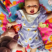 éléna participe au concours pour gagner de l'argent avec cette photo : arms, baby, bib, child, colorful, cute, face, floral_pattern, happy, head, indoor, infant, legs, lying_down, person, play_mat, plush_toy, purple_clothing, smiling, toy