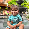 Abir is registered to the contest to win money with this photo: toddler, child, smiling, sitting, fountain, outdoor, greenery, shorts, shirt, monsters, playful, face, person, casual, daylight, public, bench, plants, cute, happy