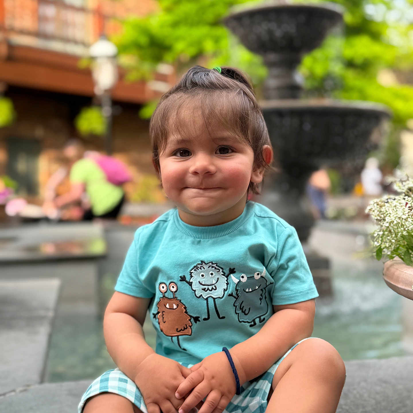 Abir is registered to the contest to win money with this photo: toddler, child, smiling, sitting, fountain, outdoor, greenery, shorts, shirt, monsters, playful, face, person, casual, daylight, public, bench, plants, cute, happy