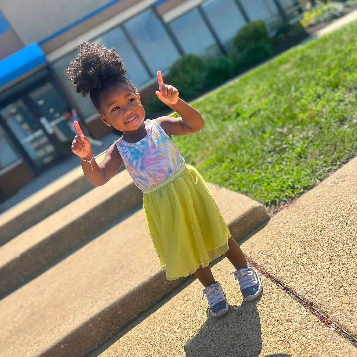 Kha'Lisia joined the competition — help win amazing prizes! child, girl, outdoor, sunny_day, sidewalk, steps, grass, building, window, shadow, pose, smiling, colorful_clothing, sneakers, hair_puff, playful, young, happy, daylight, casual