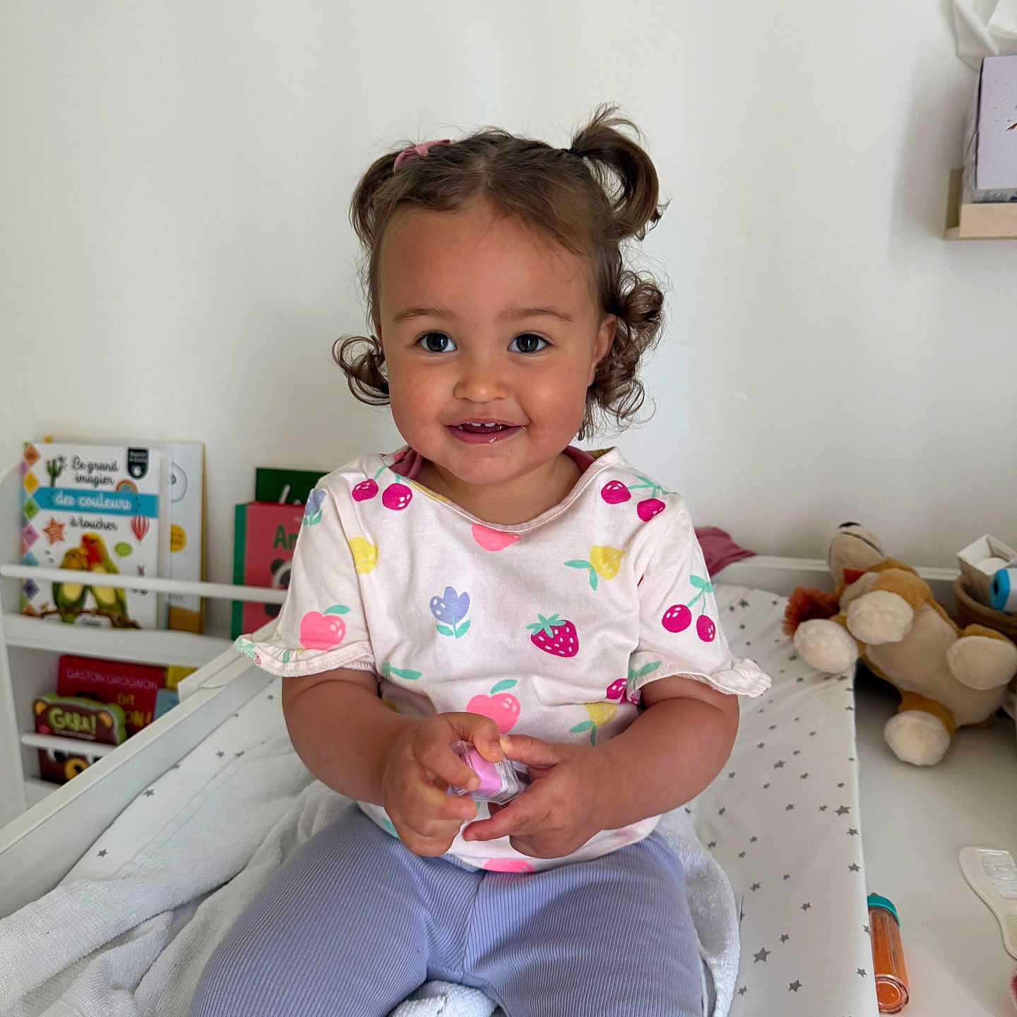 Margot a rejoint le concours — aidez-le/la à gagner de superbes lots ! baby, books, changing_pad, child, clothing, curly_hair, cute, face, furniture, hand, happy, indoor, person, pigtails, play, room, sitting, smile, toddler, toy
