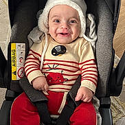 Karam a rejoint le concours — aidez-le/la à gagner de superbes lots ! baby, child, car_seat, hat, sweater, red_pants, smile, happy, indoor, footwear, stripes, seatbelt, cute, infant, clothing, face, person, toy, cozy, carrying_device