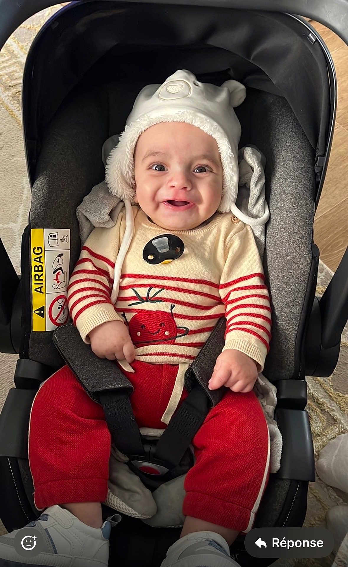Karam a rejoint le concours — aidez-le/la à gagner de superbes lots ! baby, child, car_seat, hat, sweater, red_pants, smile, happy, indoor, footwear, stripes, seatbelt, cute, infant, clothing, face, person, toy, cozy, carrying_device