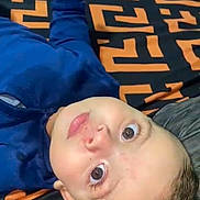Karam participe au concours pour gagner de l'argent avec cette photo : baby, blanket, blue_clothing, casual, child, closeup, curious_expression, cute, eyes, face, head, indoors, infant, lying_down, pattern, person, portrait, resting, skin, young_child