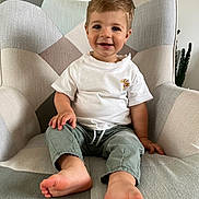 Fabio a rejoint le concours — aidez-le/la à gagner de superbes lots ! armchair, barefoot, casual_clothing, child, cute, face, furniture, green_pants, happy, home, indoor, living_room, person, plush, relaxed, sitting, smiling, toddler, white_shirt, young_child